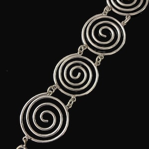May include: A silver-toned metal bracelet composed of a series of circular links, each featuring a prominent spiral design. The circular components are connected by small jump rings, and the bracelet terminates with a circular spring ring clasp.