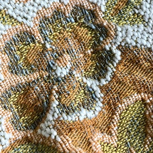May include: Close-up of a woven fabric with a textured pattern in shades of yellow, orange, white, and grey.