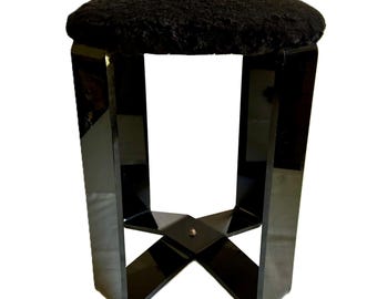 May include: A black stool with a round, textured seat and glossy, geometric legs. The legs are angled and cross near the base, creating a modern and stylish design. The stool's height is approximately 18 inches.