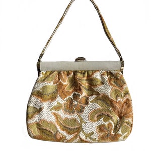 May include: A vintage clutch bag with a floral pattern in shades of gold, brown, and white. The bag has a top clasp closure and a single strap.