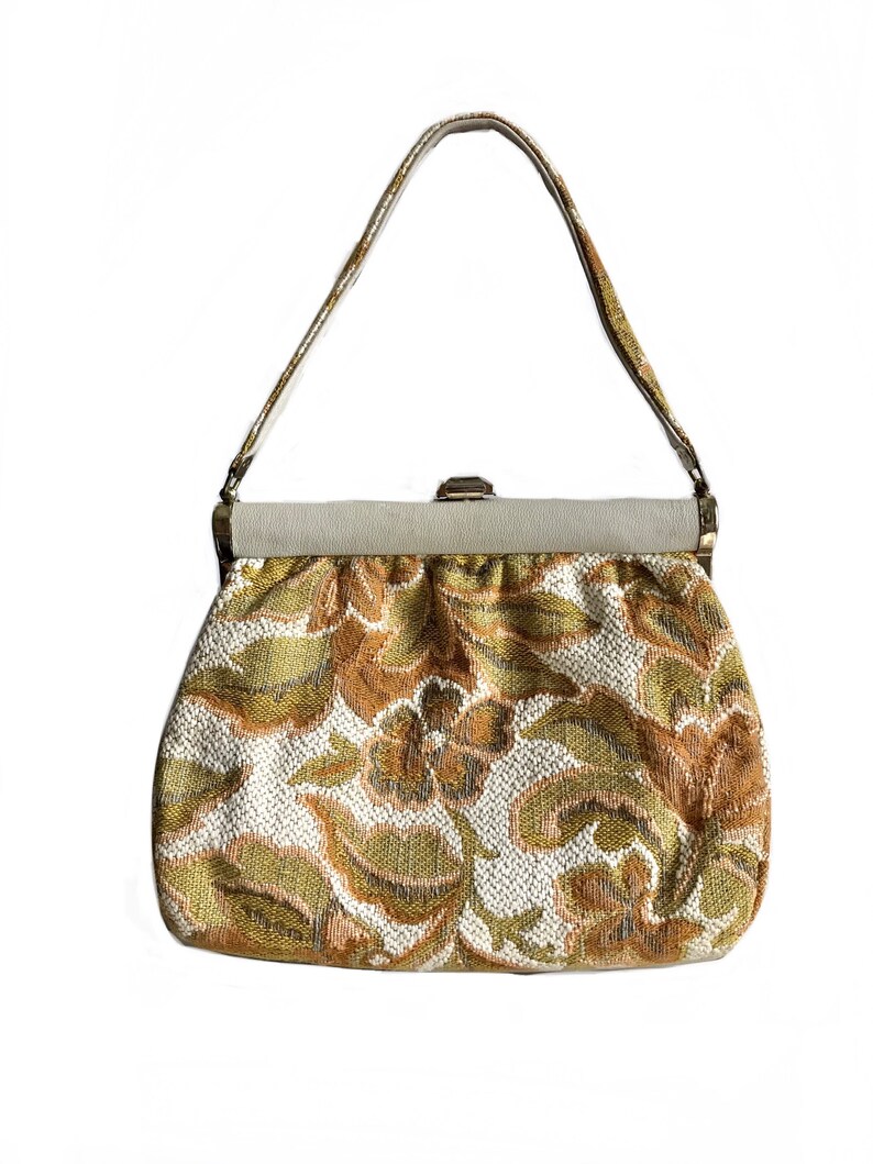 May include: A vintage clutch bag with a floral pattern in shades of gold, brown, and white. The bag has a top clasp closure and a single strap.