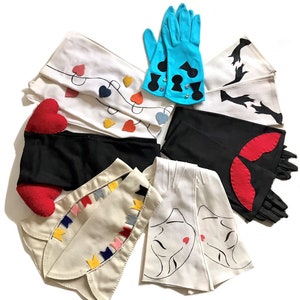May include: A collection of eight pairs of long white gloves with different decorative details. The gloves feature designs such as hearts, spades, a woman's face, and flags.