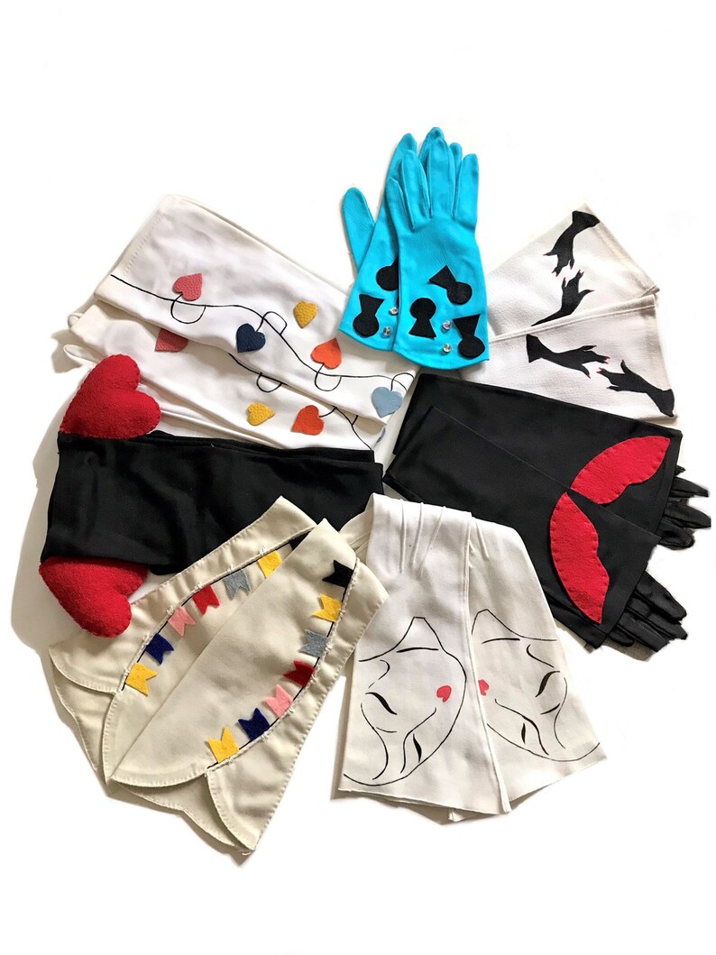 May include: A collection of eight pairs of long white gloves with different decorative details. The gloves feature designs such as hearts, spades, a woman's face, and flags.
