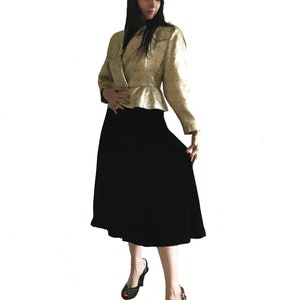 Op de afbeelding: Een vrouw draagt een jas van gouden brokaat met een zwarte fluwelen rok en zwarte schoenen. Ze draagt een zwarte hoed met een bezette rand.