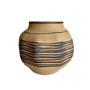 May include: A round, textured ceramic vase with a tan, sandy-colored surface. The body of the vase is decorated with horizontal, dark brown, and black wavy stripes that wrap around the center, while the rim features a solid dark brown band.