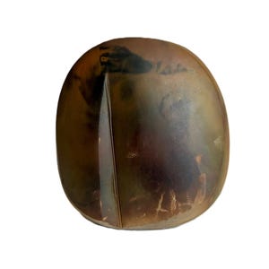 May include: A smooth, rounded, pebble-shaped object with a polished surface. The color is a gradient of deep brown, amber, and dark charcoal tones, featuring a distinct vertical line or seam running down the center of the front face.