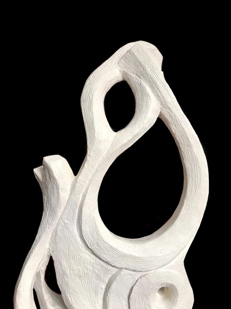 Pode incluir: Uma escultura branca com superf&iacute;cie texturizada apresentando linhas org&acirc;nicas fluidas e um grande espa&ccedil;o aberto central. A forma consiste em segmentos curvos interconectados que criam uma figura abstrata cont&iacute;nua sobre um fundo preto.