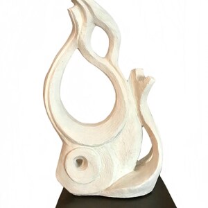 Pode incluir: Uma escultura abstrata em tom esbranqui&ccedil;ado com uma superf&iacute;cie texturizada e linhas esculpidas vis&iacute;veis. A pe&ccedil;a tem uma forma alta, curva e semelhante a uma chama, com um espa&ccedil;o central aberto e um recorte circular perto da base.