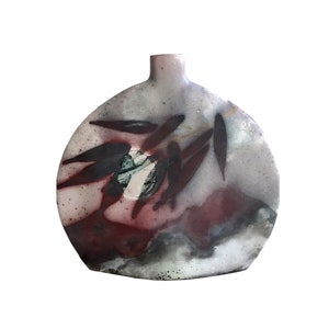 May include: A round ceramic vase with a gray, white, and red glaze. The vase has a unique design with a branch of leaves painted on the front.
