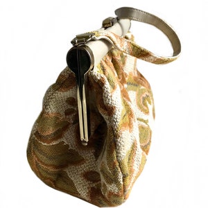 May include: A vintage style clutch bag with a floral pattern in shades of beige, green, and brown. The bag has a top clasp closure and a single handle.