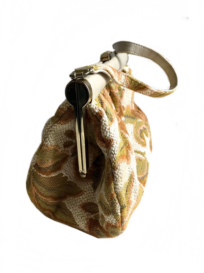 May include: A vintage style clutch bag with a floral pattern in shades of beige, green, and brown. The bag has a top clasp closure and a single handle.