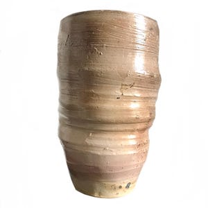 Könnte beinhalten: Eine hohe, zylindrische Keramikvase mit hellbrauner Glasur. Die Vase hat eine strukturierte, leicht unebene Oberfläche und ein dezentes, gestreiftes Muster.