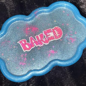 May include: A cloud-shaped tray with a glittery blue surface and a bright blue rim. The tray has pink accents and the word "BAKED" in pink and white lettering.