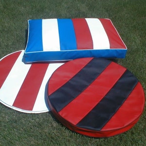 May include: Three pieces of outdoor furniture: a rectangular pillow and two round cushions. The pillow has red, white, and blue stripes. One cushion has red and white stripes, and the other has red and black stripes. All pieces have white trim.