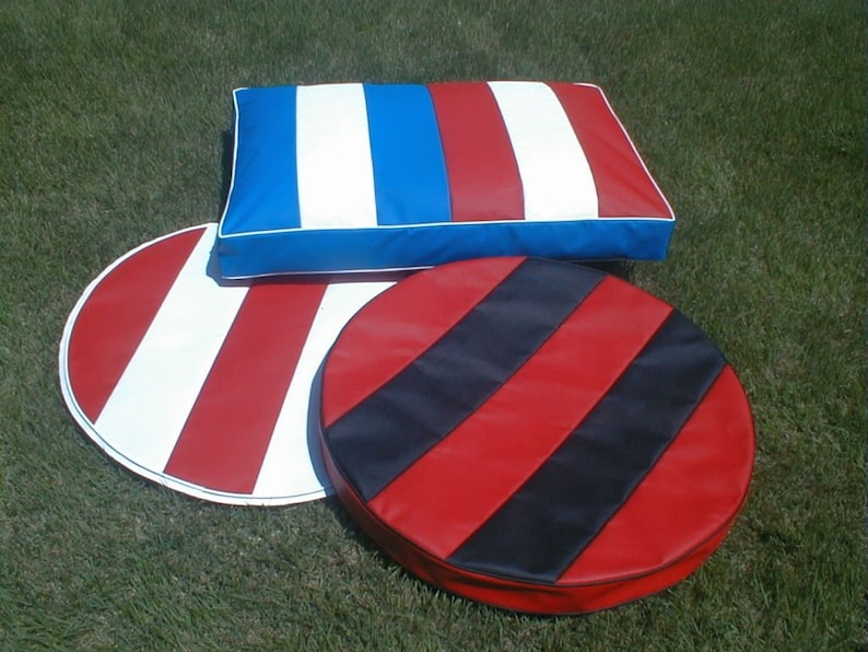 May include: Three pieces of outdoor furniture: a rectangular pillow and two round cushions. The pillow has red, white, and blue stripes. One cushion has red and white stripes, and the other has red and black stripes. All pieces have white trim.