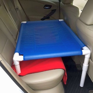 May include: A blue mesh dog bed suspended over the back seat of a car using white PVC pipes. The bed is supported by two pipes on each side. A red blanket is on the back seat below the bed.