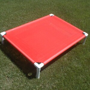 May include: A red elevated dog bed with a white frame. The bed is made of a durable fabric and is designed to keep pets cool and comfortable.