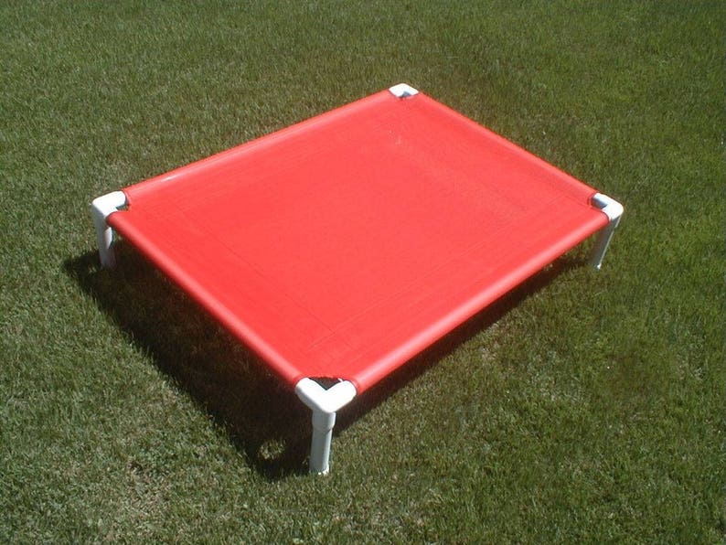May include: A red elevated dog bed with a white frame. The bed is made of a durable fabric and is designed to keep pets cool and comfortable.