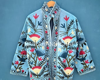May include: A light blue velvet jacket with intricate floral embroidery in red, yellow, blue, and green. The jacket features a high collar and a button closure. The embroidery design includes stylized flowers and leaves.