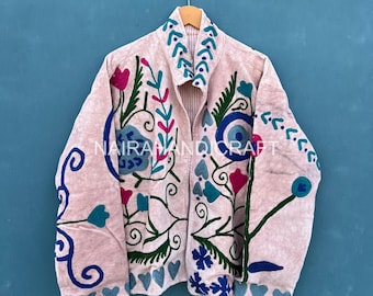 May include: A light pink jacket with intricate floral embroidery in shades of green, blue, and pink. The jacket features a collared neckline and is hanging against a blue background. The text "NAIRAMANDICRAFT" is visible on the jacket.