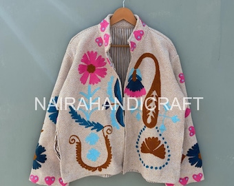 May include: Beige jacket with colorful floral embroidery. The jacket features pink, blue, and brown embroidered designs, including flowers and paisley shapes. The text "NAIRAHANDICRAFT" is visible on the front of the jacket.