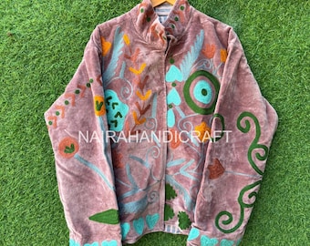 May include: A mauve velvet jacket with colorful floral embroidery. The jacket features turquoise, orange, and green embroidered designs, with the text "NA RAHANDICRAFT" visible. The jacket is hanging on a wooden hanger against a green grass background.