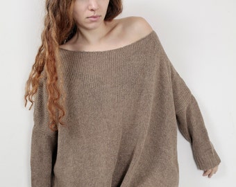 May include: A brown oversized knitted sweater with a slightly off-the-shoulder neckline. The sweater is worn with ripped blue jeans.