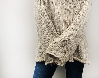 Może przedstawiać: Beżowy sweter z dzianiny w rozmiarze oversize o luźnym, wygodnym kroju. Sweter ma okrągły dekolt i długie rękawy. Dzianina jest w jasnobeżowym kolorze, a rękawy są długie i szerokie. Sweter jest połączony z niebieskimi dżinsami.