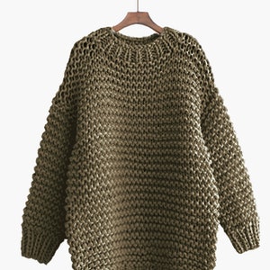 May include: A chunky knit sweater in a muted olive green color. The sweater has a relaxed fit and a round neckline.