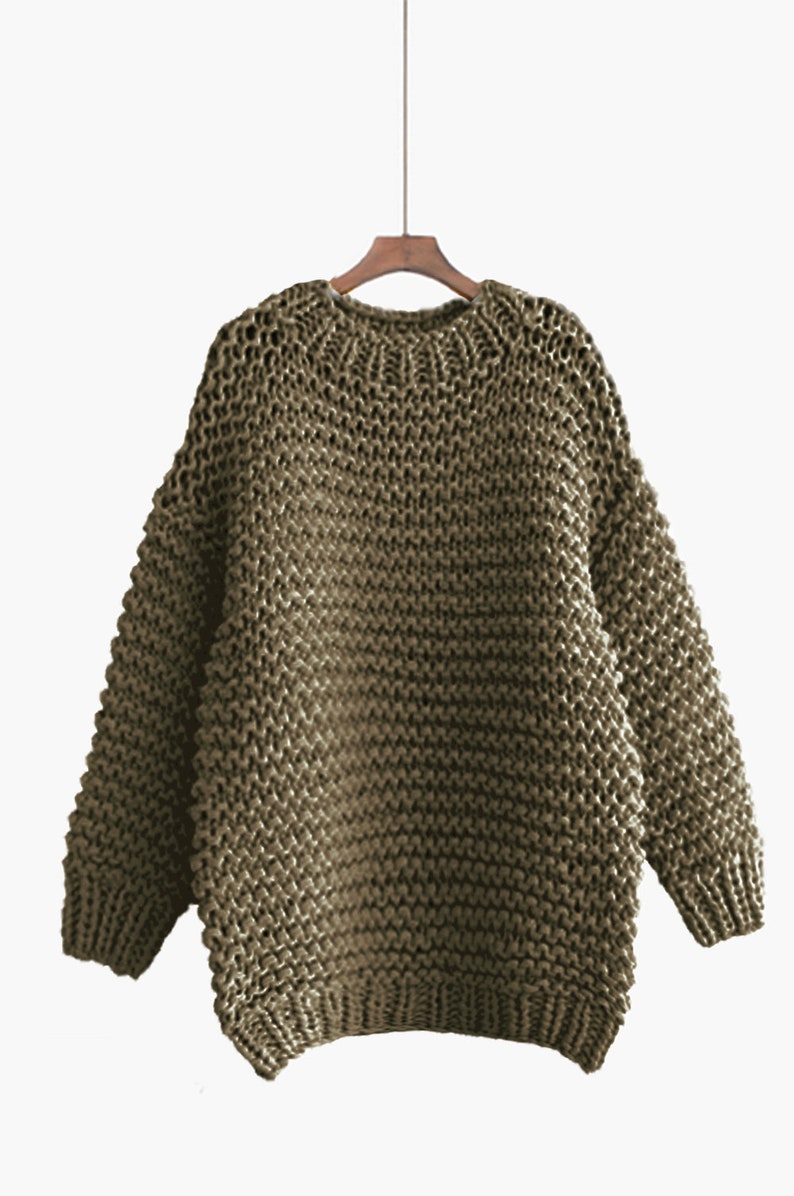 May include: A chunky knit sweater in a muted olive green color. The sweater has a relaxed fit and a round neckline.
