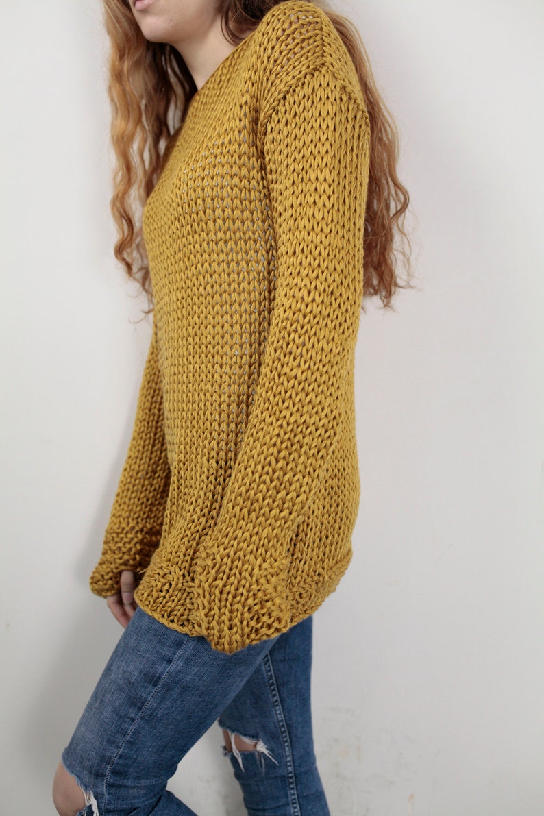 May include: A mustard yellow knitted sweater with long sleeves and a loose fit.