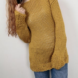 May include: A loose-fitting, mustard yellow knitted sweater with long sleeves. The sweater is made of a chunky yarn and has a relaxed, casual fit.