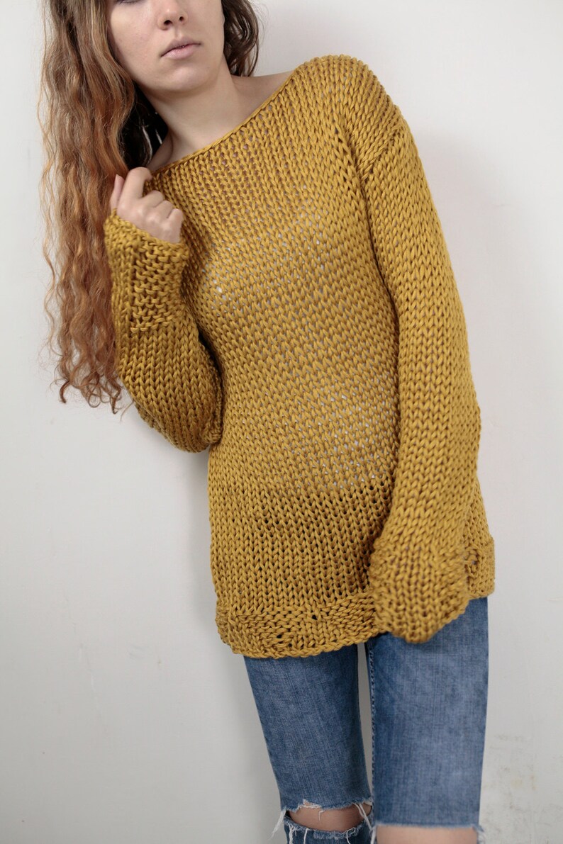May include: A loose-fitting, mustard yellow knitted sweater with long sleeves. The sweater is made of a chunky yarn and has a relaxed, casual fit.