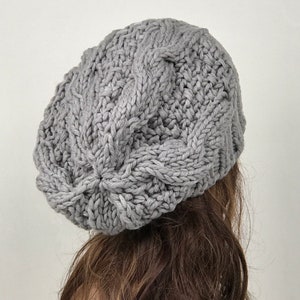May include: A gray knitted beanie with a cable knit pattern.