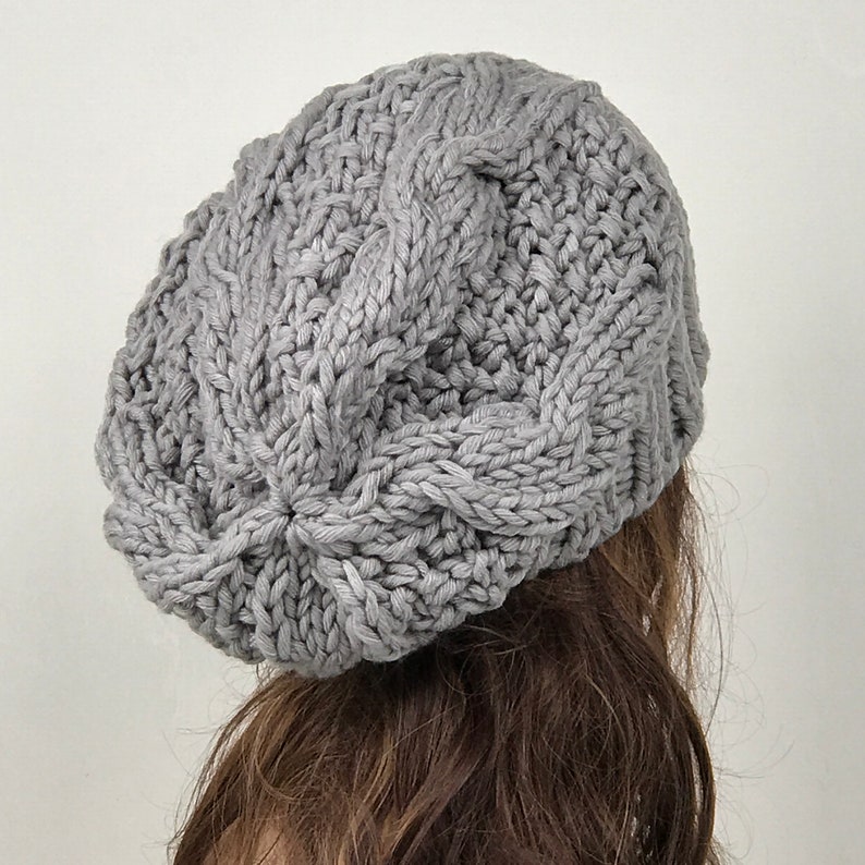 May include: A gray knitted beanie with a cable knit pattern.