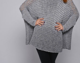 May include: A gray knitted sweater with a loose, oversized fit. The sweater has a wide, round neckline and long sleeves.