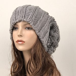 May include: A gray slouchy beanie hat made of knitted wool. The hat has a cable knit pattern and a slouchy fit.