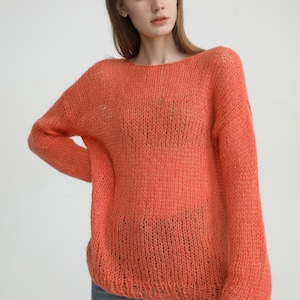 May include: A loose-fitting, coral-colored knitted sweater with a slightly open neckline. The sweater is made of a soft, airy yarn and has a relaxed, casual fit.