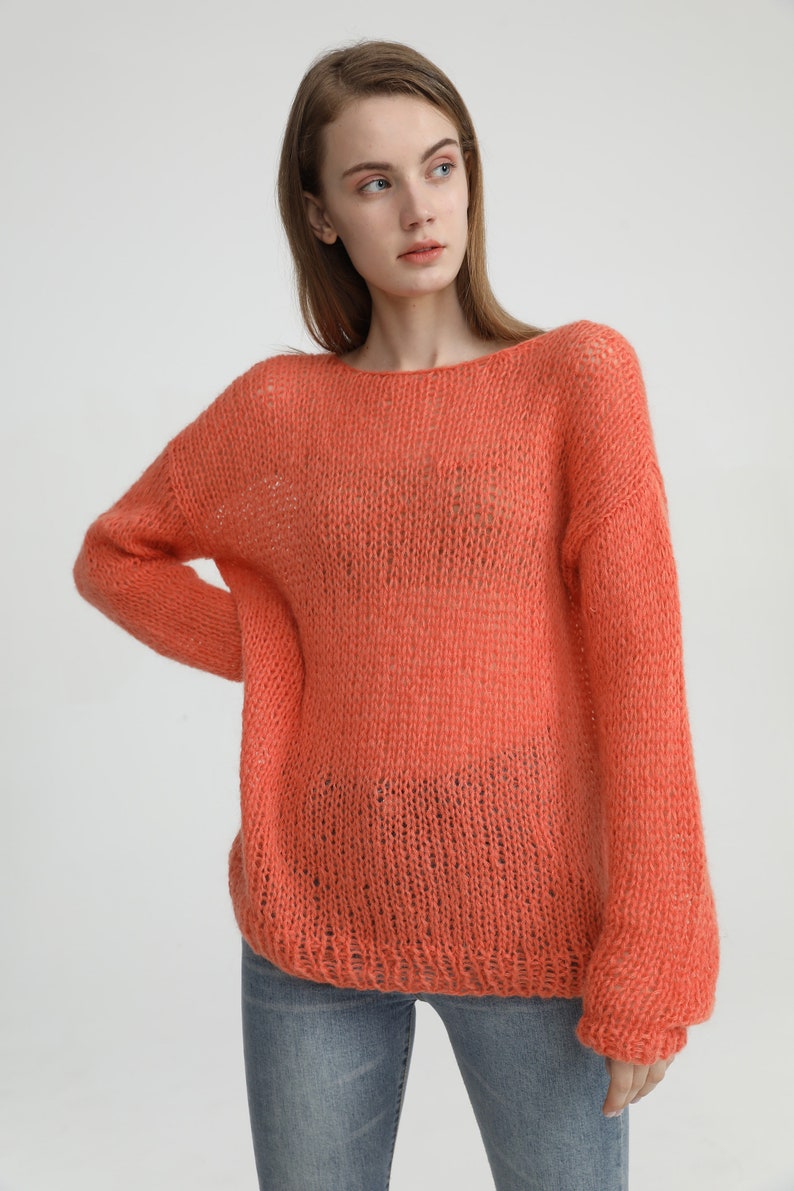 May include: A loose-fitting, coral-colored knitted sweater with a slightly open neckline. The sweater is made of a soft, airy yarn and has a relaxed, casual fit.