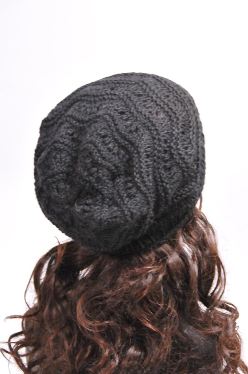 May include: A black knitted beanie with a cable knit pattern. The beanie is worn on a mannequin with long brown curly hair.