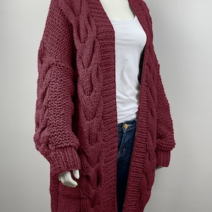 May include: A long, burgundy cable knit cardigan with a V-neck and long sleeves.