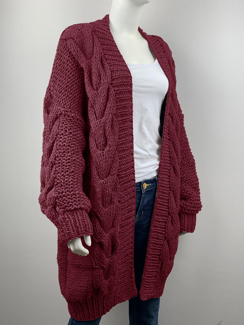 May include: A long, burgundy cable knit cardigan with a V-neck and long sleeves.