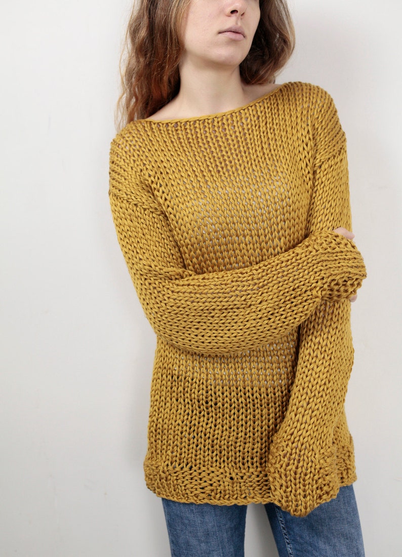 May include: A loose-fitting, mustard yellow knitted sweater with a wide neckline and long sleeves.