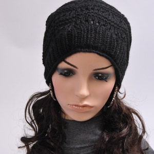 May include: A black knit beanie with a simple stitch pattern. The beanie is worn by a mannequin with long, dark brown curly hair and large hoop earrings.