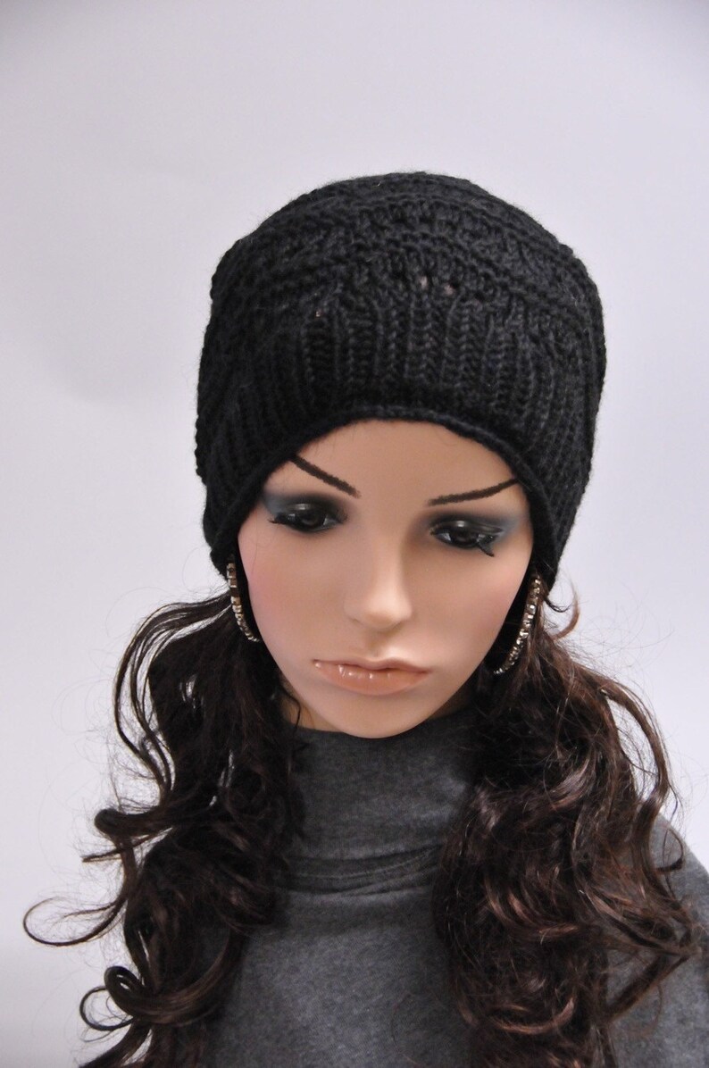 May include: A black knit beanie with a simple stitch pattern. The beanie is worn by a mannequin with long, dark brown curly hair and large hoop earrings.