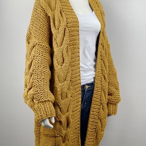 May include: A long, mustard yellow cardigan with a cable knit pattern and oversized sleeves.