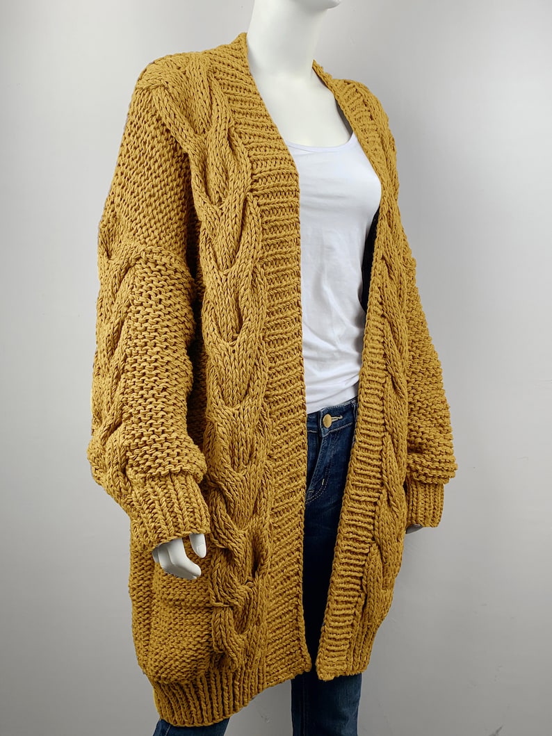 May include: A long, mustard yellow cardigan with a cable knit pattern and oversized sleeves.