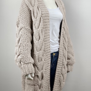May include: A long, beige cable knit cardigan with a relaxed fit and oversized sleeves. The cardigan is open in the front and has a V-neck.