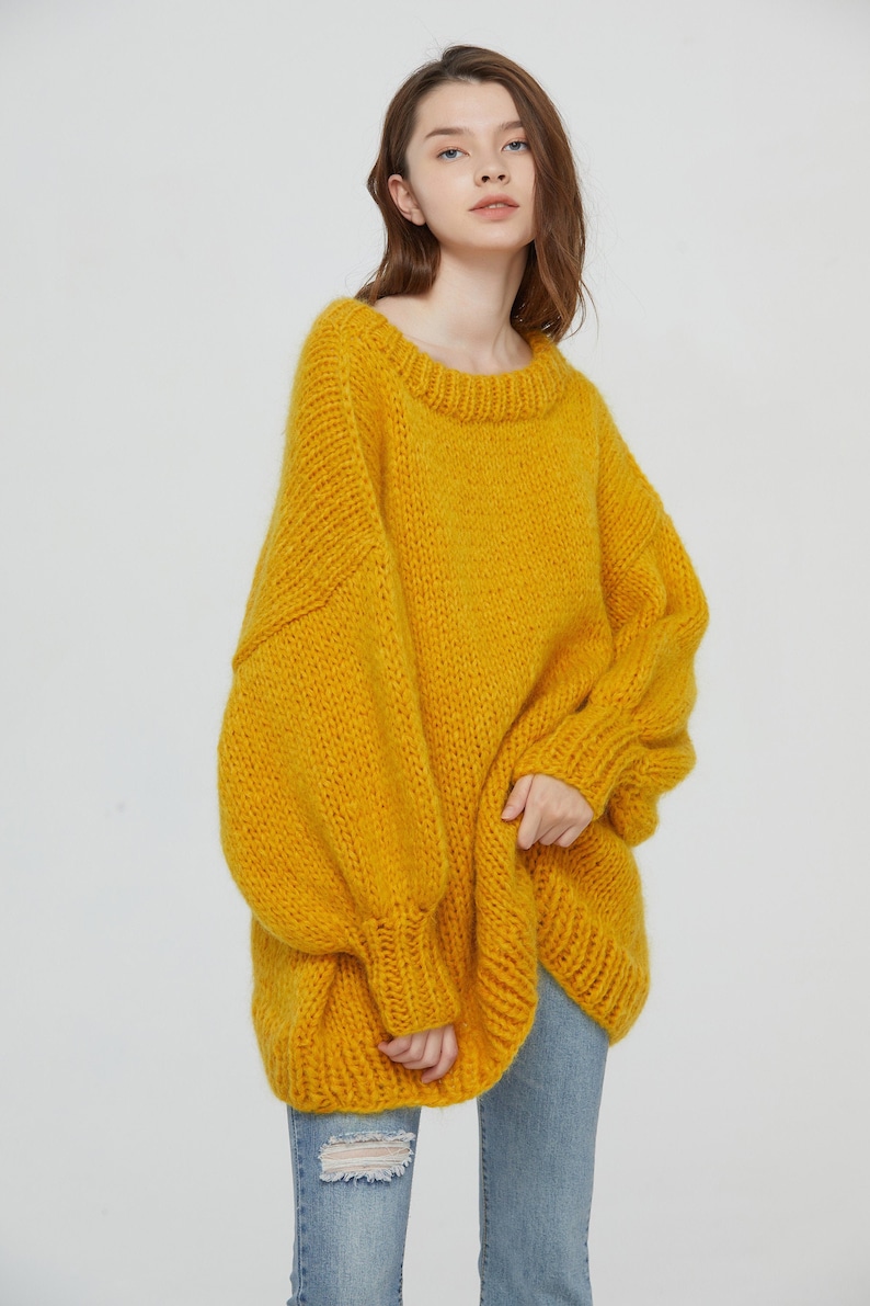 K&ouml;nnte beinhalten: Ein &uuml;bergro&szlig;er gelber Strickpullover mit Rundhalsausschnitt. Der Pullover ist aus weichem, dickem Garn gefertigt und hat eine lockere Passform.