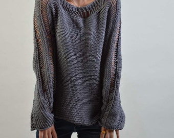 May include: A gray knitted sweater with a loose fit and openwork detailing on the sleeves. The sweater has a wide neckline and a relaxed silhouette.